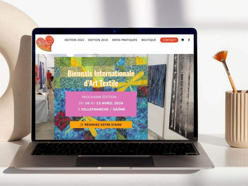 Page d'accueil du site e-commerce de la Biennale Internationale d'Art Textile avec en fond une exposition d'oeuvres d'artistes et au premier plan les dates de la prochaine édition